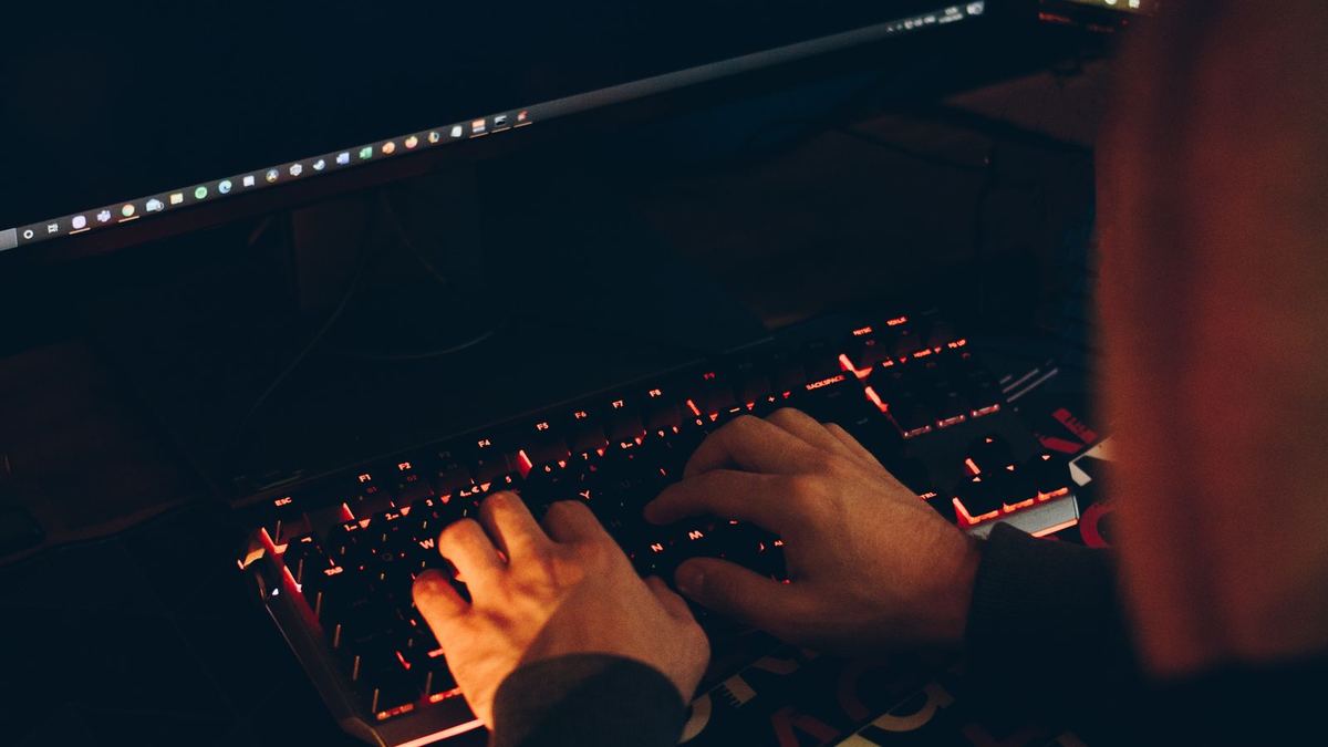 Persona escribiendo en un teclado retroiluminado en la oscuridad